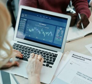 Business professionals analyzing financial data on a laptop during a meeting. Charts and reports visible.