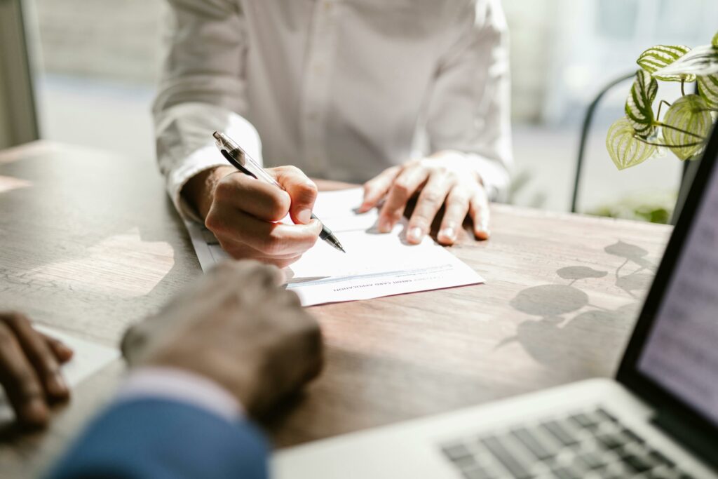 Close-up of people signing a document at a desk, highlighting professional business interaction.